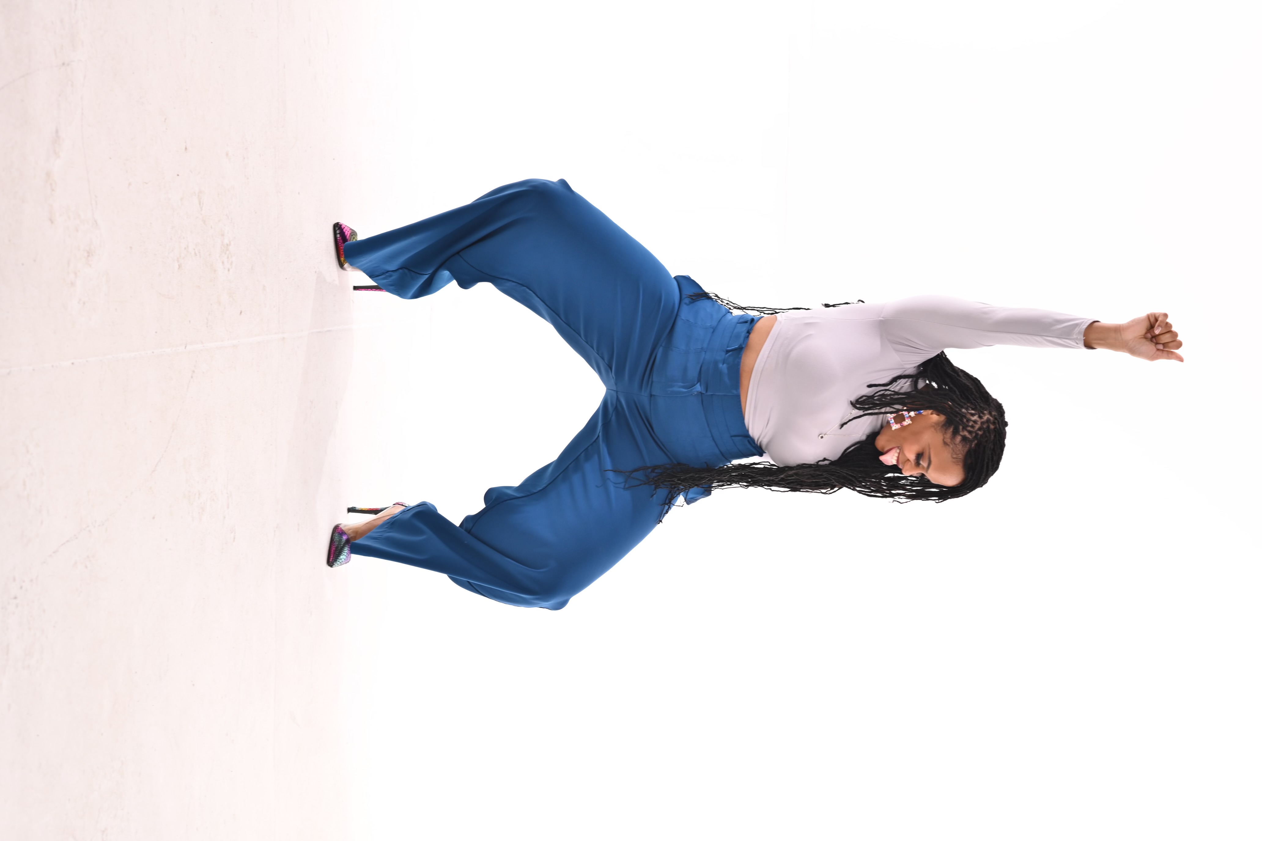 Akilah in a playful pose with her arm raised, wearing blue trousers